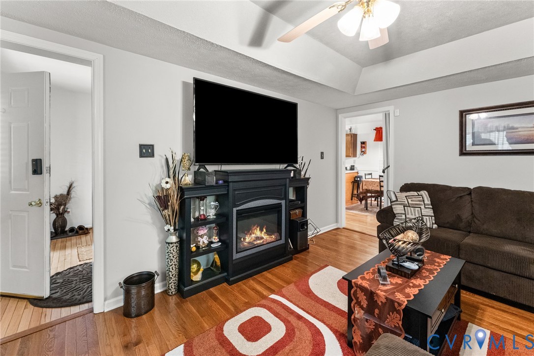 Tray ceiling, wood-finish flooring, and built-in fireplace mantle with integrated shelving
