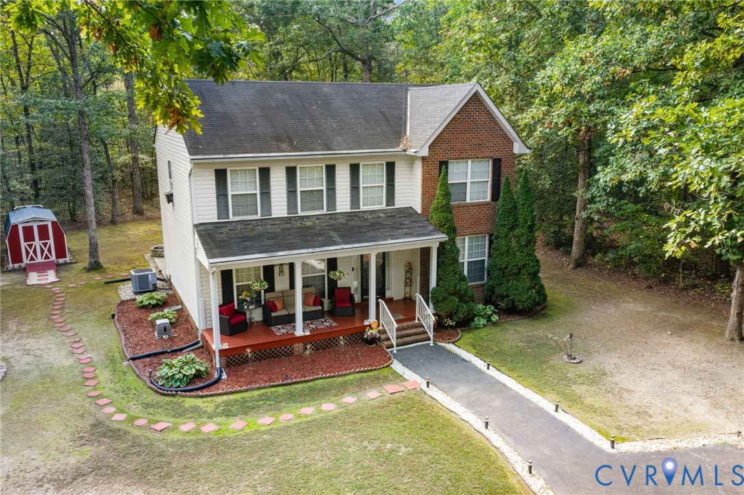 Two-story exterior featuring a brick and siding facade, covered front porch with columns, asphalt shingle roof, stone walkway, and detached storage structure