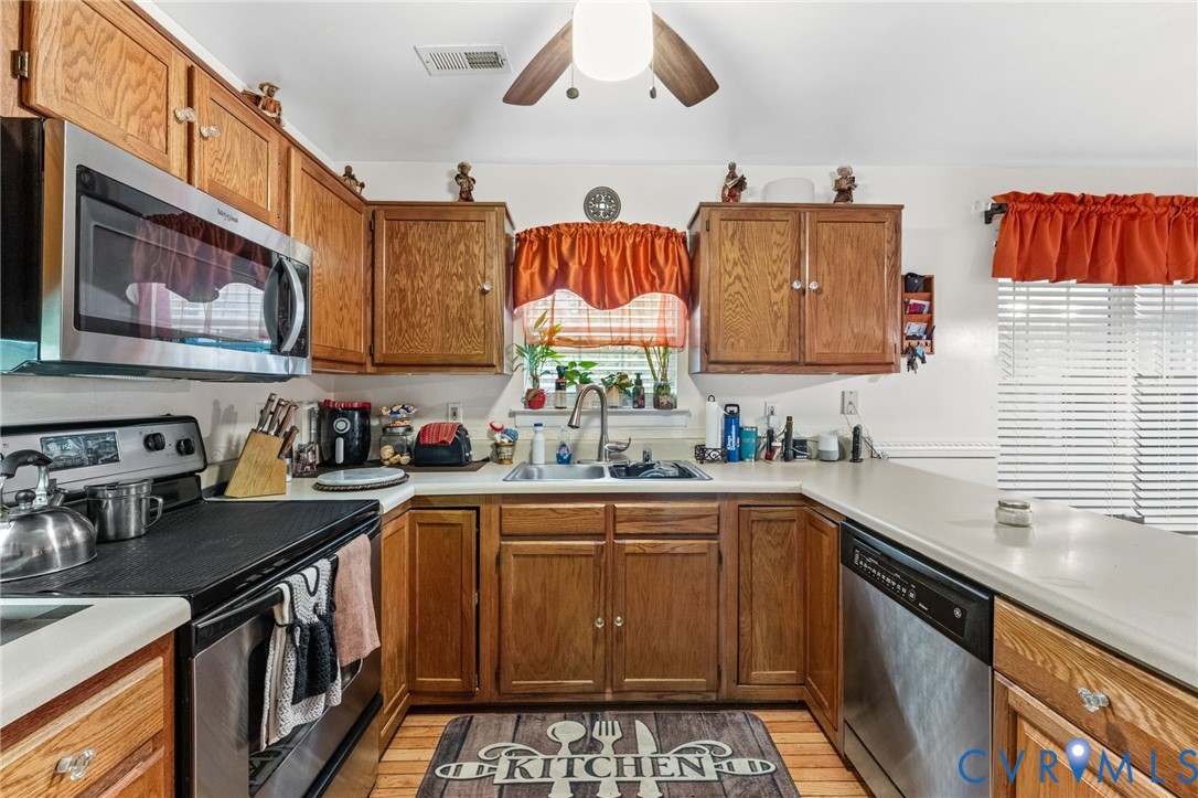 Kitchen featuring wood cabinetry, stainless steel appliances, dual-basin sink with arched faucet, and solid-surface countertops