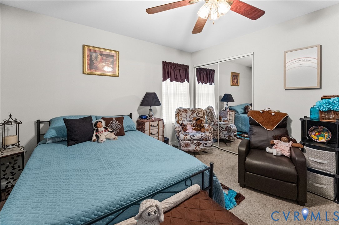 Bedroom featuring wall-to-wall carpeting, dual-pane windows, a sliding mirrored closet door, and an attached multi-light ceiling fan