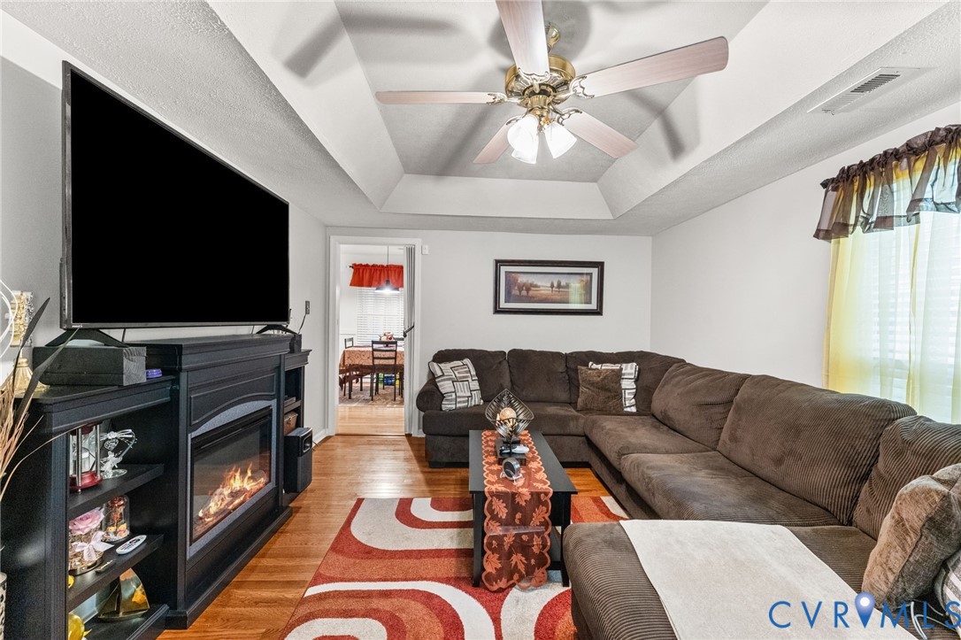Tray ceiling, wood-finish flooring, and built-in fireplace featuring a black mantel