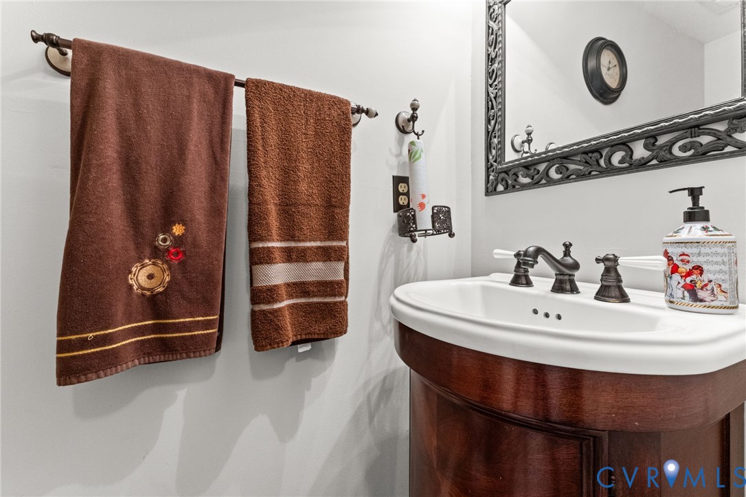 Curved wood vanity cabinet with white ceramic basin, dark-finish widespread faucet, and decorative wall-mounted mirror