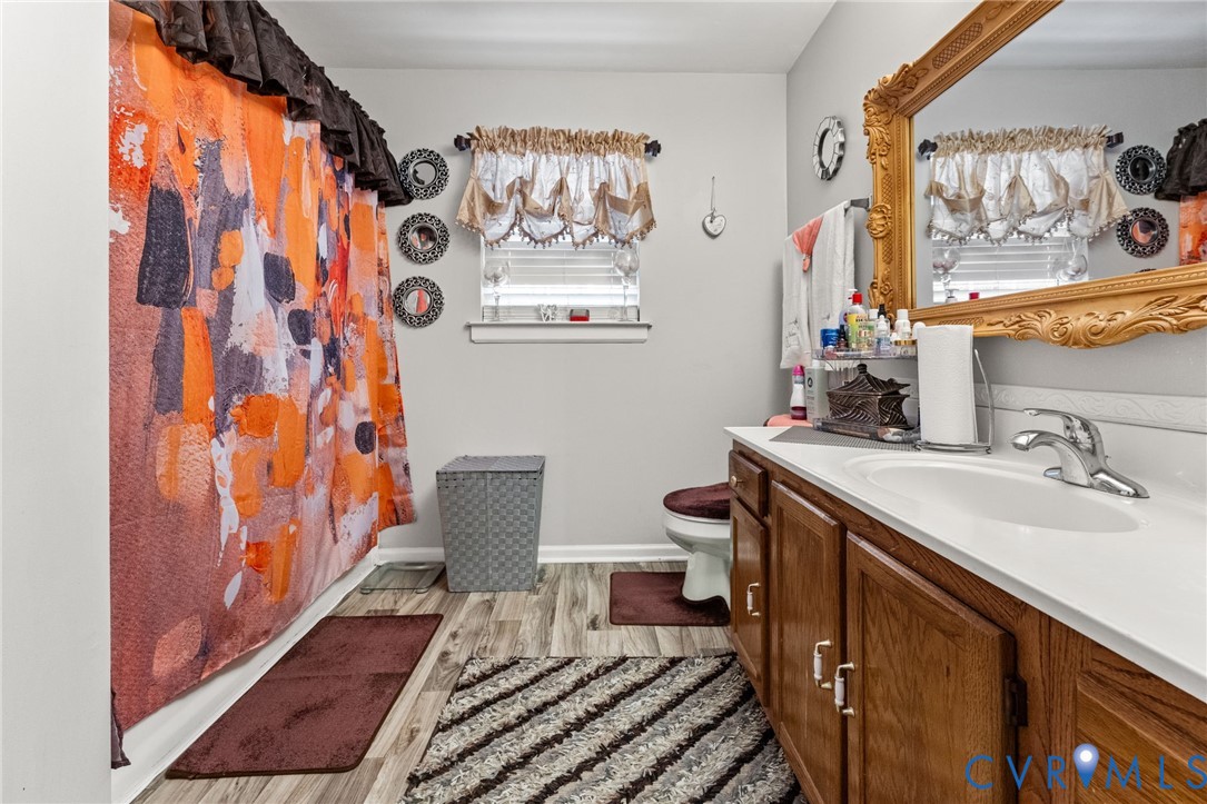 Bathroom featuring a single-sink vanity with wood-finish cabinetry, an integrated white countertop, wood-finish flooring, and a window