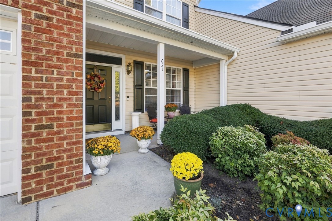 Covered front entryway featuring a brick facade, vinyl siding, shutter-accented windows, and a concrete walkway Covered front entryway featuring a brick facade, vinyl siding, shutter-accented windows, and a concrete walkway