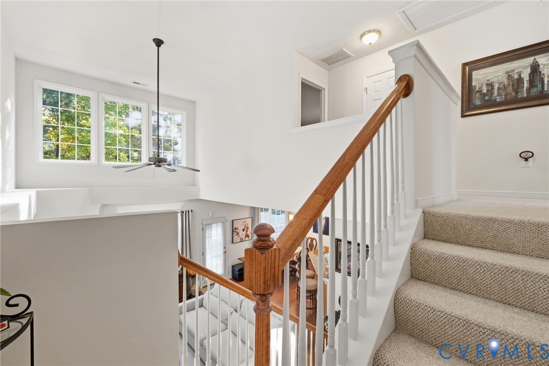 Staircase featuring a wooden handrail, white balusters, and carpeted treads, complemented by high-reaching windows and a ceiling-mounted fan