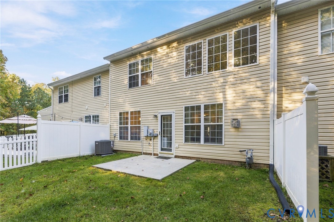 Rear exterior featuring vinyl siding, multi-pane windows, concrete patio, and white vinyl privacy fencing