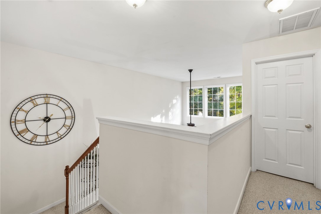 Neutral-toned interior featuring carpeting, a white paneled door, and a staircase with a wooden handrail and white balusters