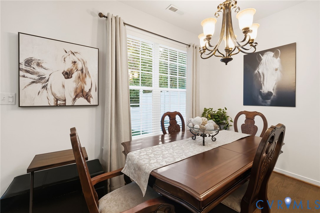 Dining area featuring wood-finish flooring, a multi-arm chandelier, and double-hung windows with horizontal blinds