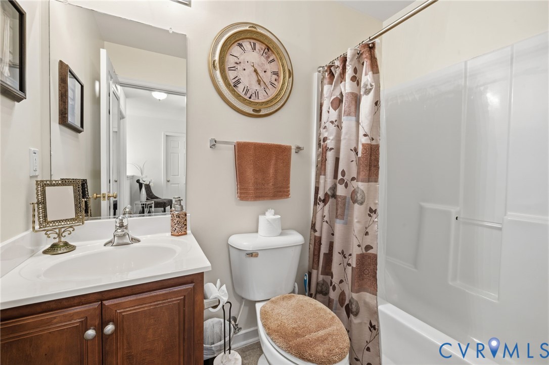 Bathroom featuring a wood-finish vanity with a white countertop and integrated sink, a large wall-mounted mirror, and a full-height acrylic tub and shower surround