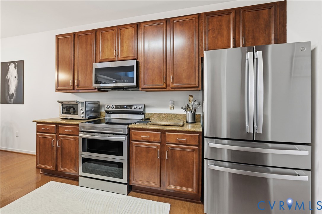 Kitchen featuring stained-wood cabinetry, stone countertops, and stainless steel appliances including a double-oven range, over-the-range microwave, and French-door refrigerator