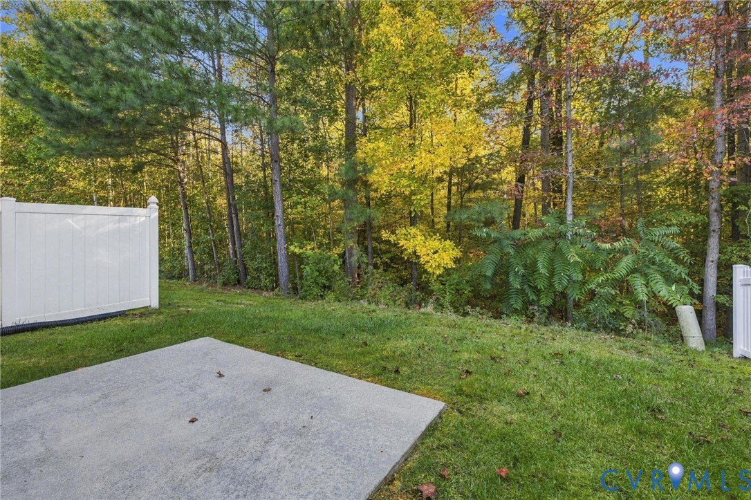 Concrete patio featuring a manicured lawn, white vinyl fencing, and mature trees