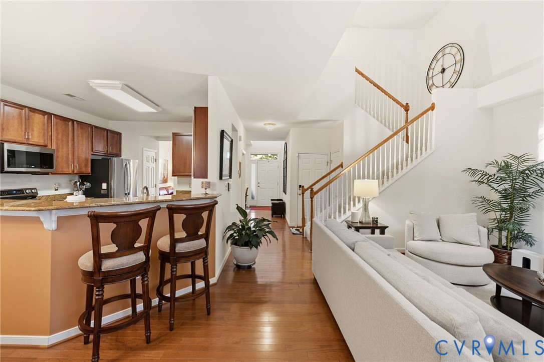 Open-concept floor plan featuring wood-finish flooring, a kitchen breakfast bar with stone-surfaced countertops, custom wood cabinetry, and a staircase with a wooden banister