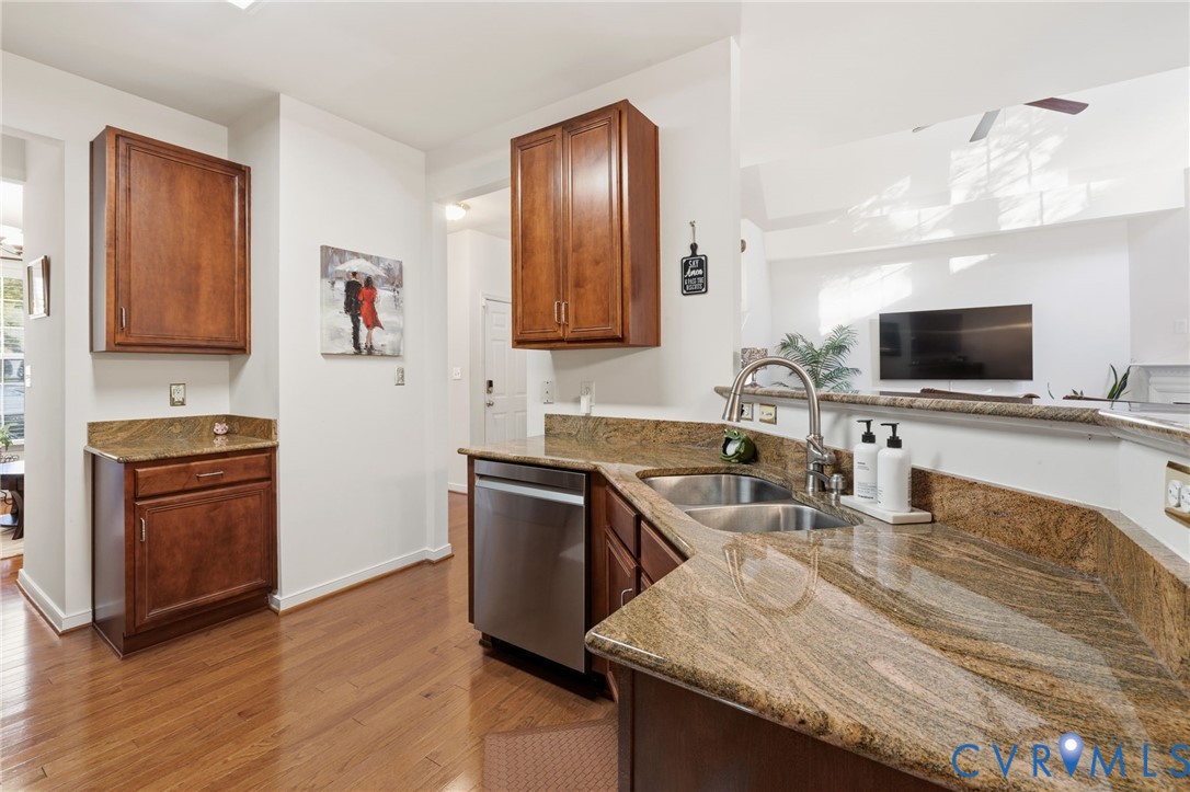 Kitchen featuring stained wood cabinetry, stone-surface countertops, wood-finish flooring, and a stainless steel dishwasher with a dual-basin undermount sink