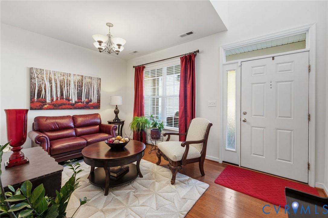 Foyer and room featuring wood-finish flooring, a multi-light chandelier, a multi-paneled entry door with side light and transom window, and a window with wood blinds