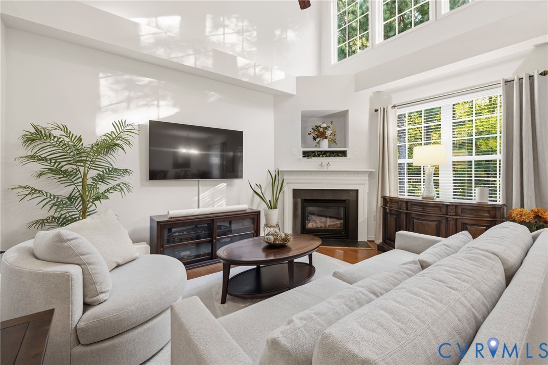 Living area featuring a high vaulted ceiling, fireplace with a mantel, built-in wall niche, oversized windows, and wood-finish flooring