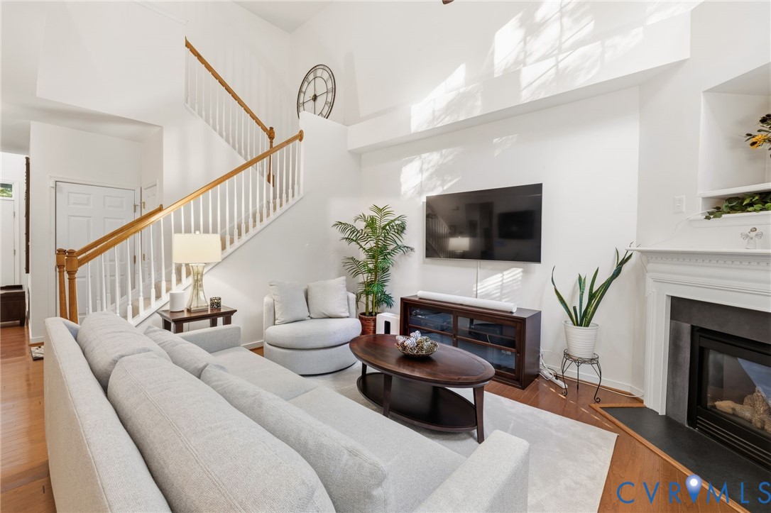 Living area featuring vaulted ceilings, a fireplace with a mantel and stone-finish surround, wood-finish flooring, and a staircase with a wooden handrail and balusters