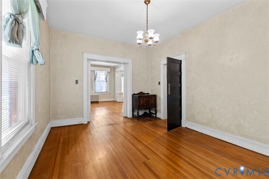 Interior room featuring wood-finish flooring, textured wall finishes, a five-panel solid wood door, and a multi-arm metal chandelier