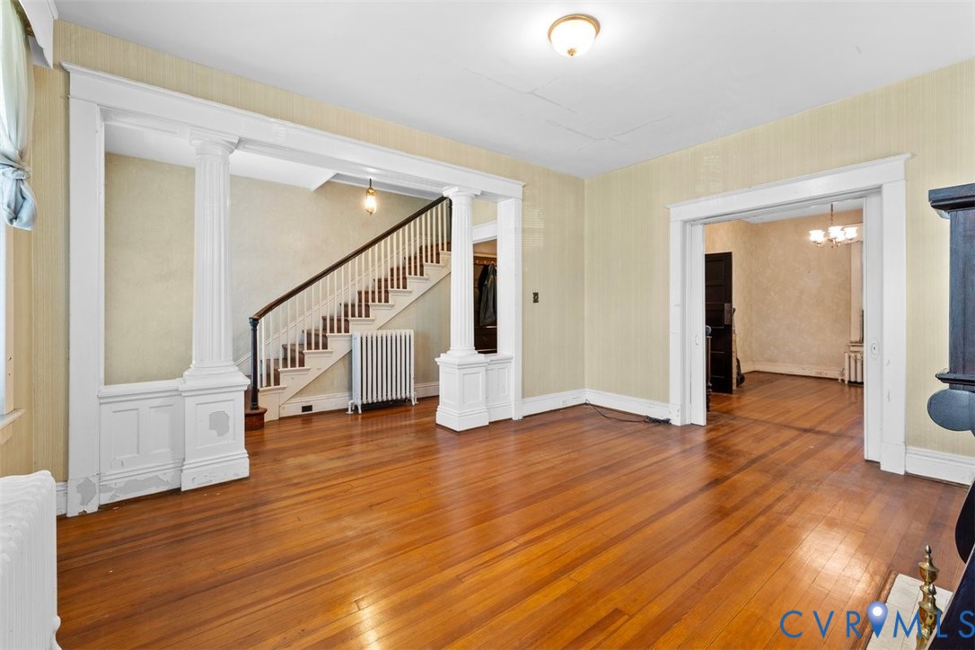 Interior space featuring wood-finish flooring, architectural columns with wainscoting detail, a staircase with a wooden handrail, and prominent millwork trim throughout the entries