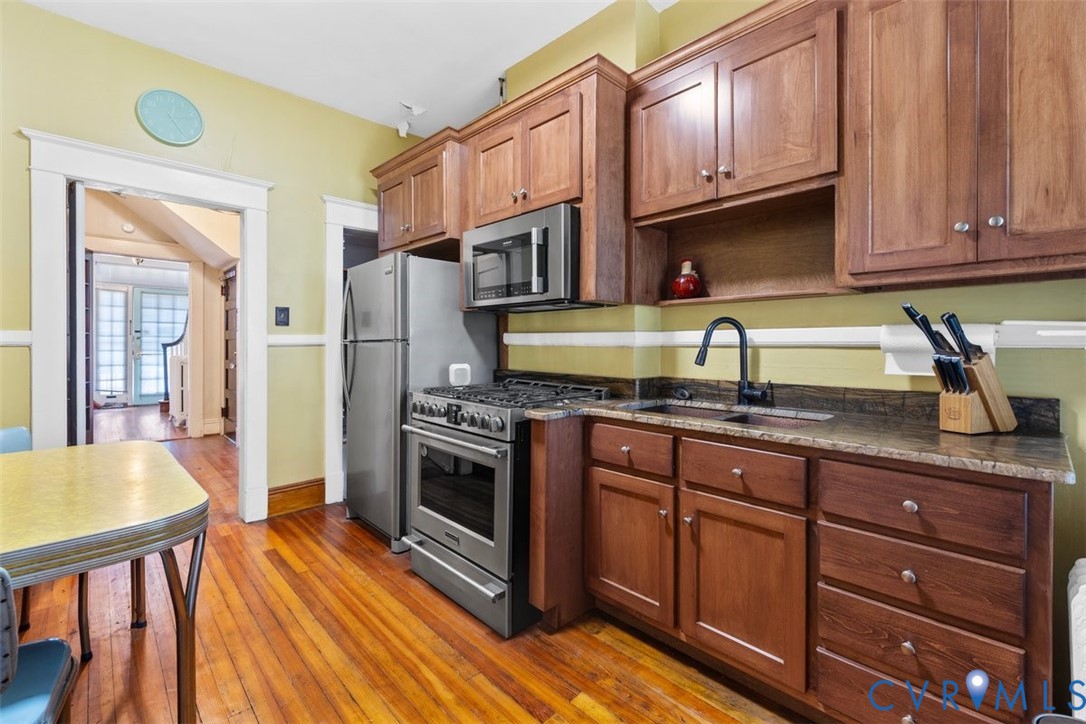 Kitchen featuring shaker-style wood cabinetry, stainless steel gas range, integrated microwave, stone-finish countertops, and wood-finish flooring