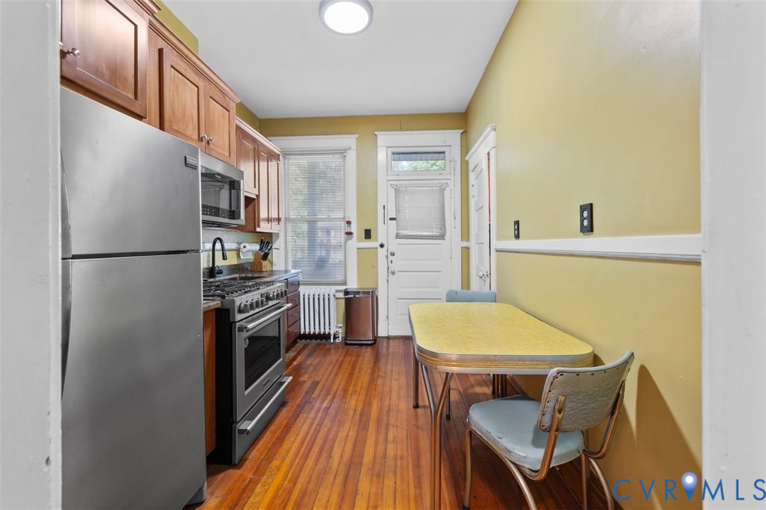 Kitchen featuring wood-finish flooring, stainless steel appliances, stained wood cabinetry, and a high-arch faucet