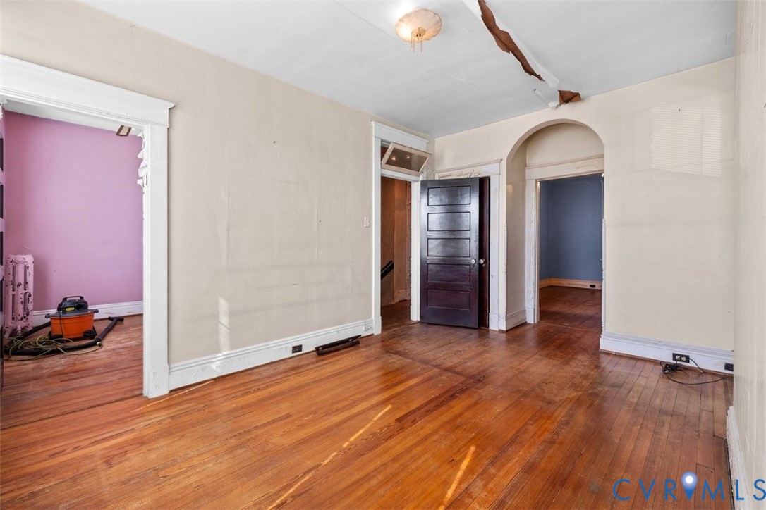 Primary bedroom featuring wood-finish flooring, historic wood-paneled door, arched doorway, and classic millwork trim