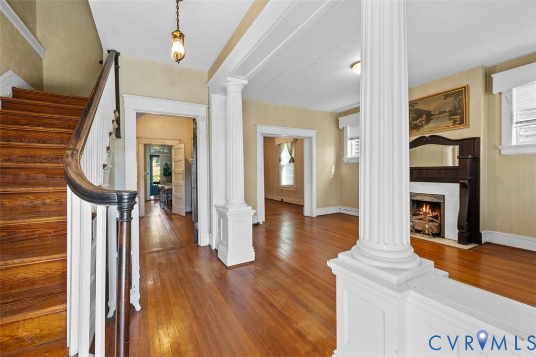 Interior entry featuring wood-finish flooring, classic fluted columns, a wood staircase with a curved banister, and a fireplace with a built-in mantel