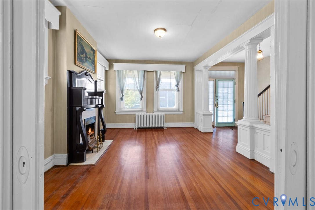 Hardwood flooring, decorative fireplace with an ornate mantel, classic architectural columns, and multi-pane entry door