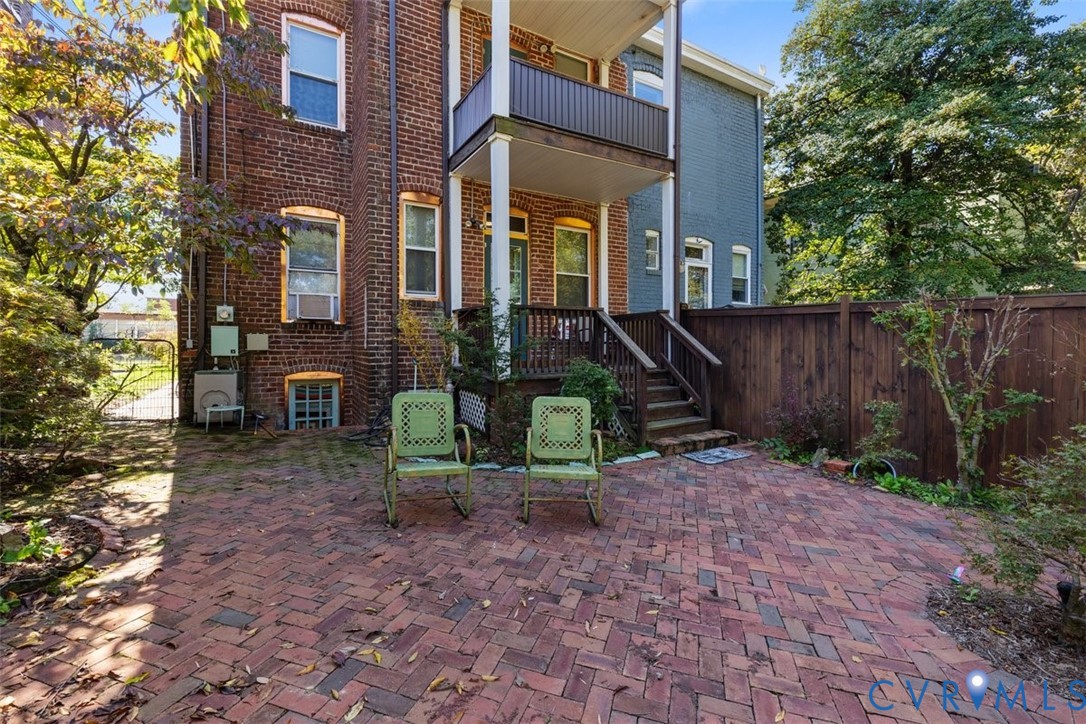 Herringbone-pattern brick patio featuring an elevated wooden deck, wood privacy fencing, and a red brick exterior facade