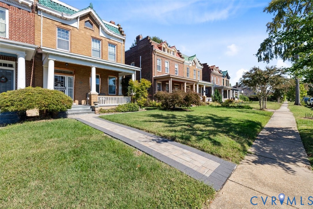 Brick exterior featuring a covered front porch, white columns, decorative roofline gables, and a stone-paver walkway