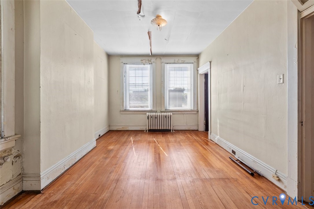 Primary bedroom with wood-finish flooring, dual windows with decorative molding, and a cast-iron radiator