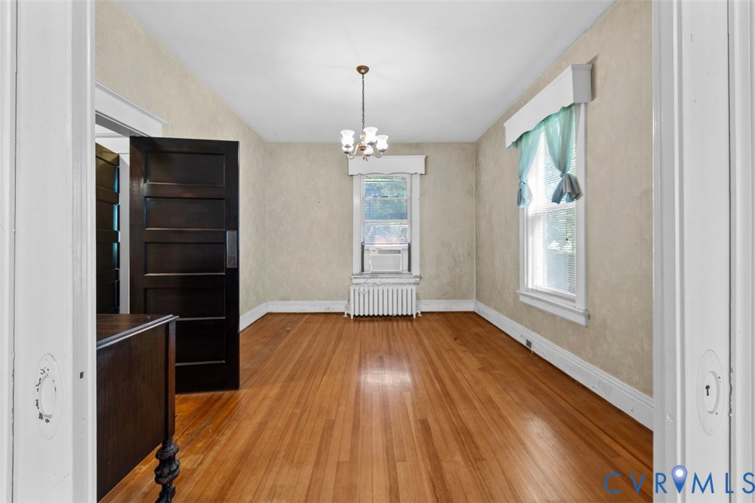 Hardwood flooring, multi-panel dark wood door, and central chandelier light fixture