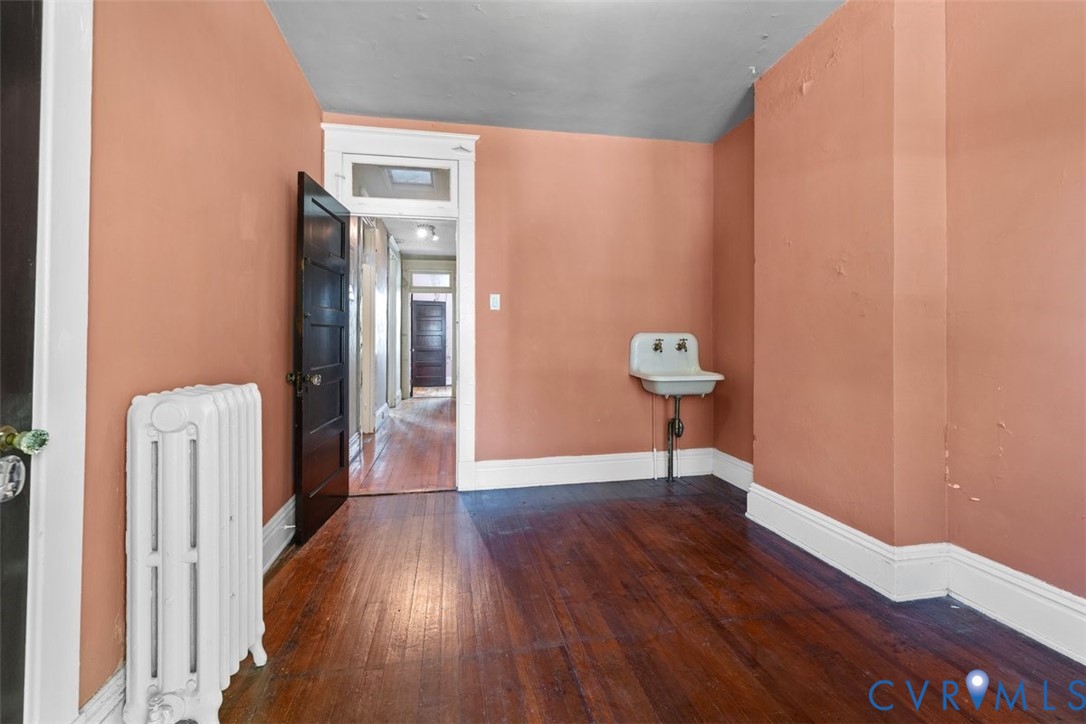 Third bedroom with wall-mounted basin, cast iron radiator, and solid wood interior door with transom window