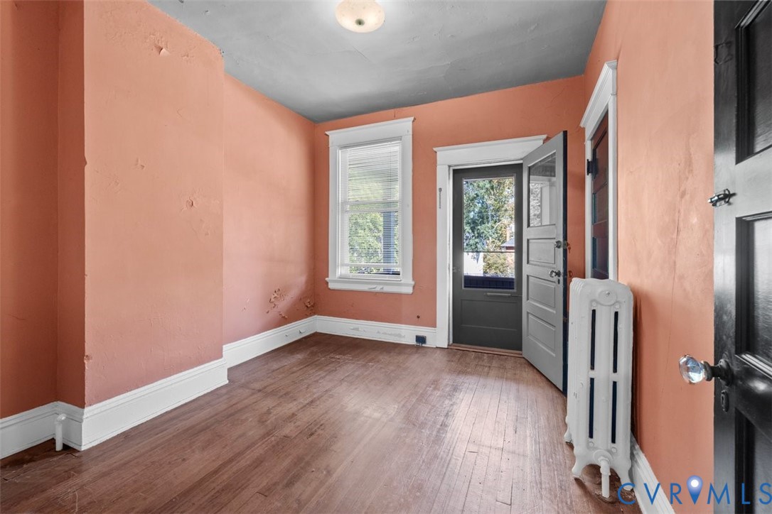 Third bedroom featuring wood-finish flooring, a white cast-iron radiator, a single-pane window with white trim, and a black-finished door with an integrated window pane