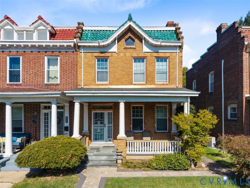 Brick facade exterior featuring a covered front porch with classic columns, a prominent green tile roof accent, stone-paved entry, and white decorative railing Brick facade exterior featuring a covered front porch with classic columns, a prominent green tile roof accent, stone-paved entry, and white decorative railing