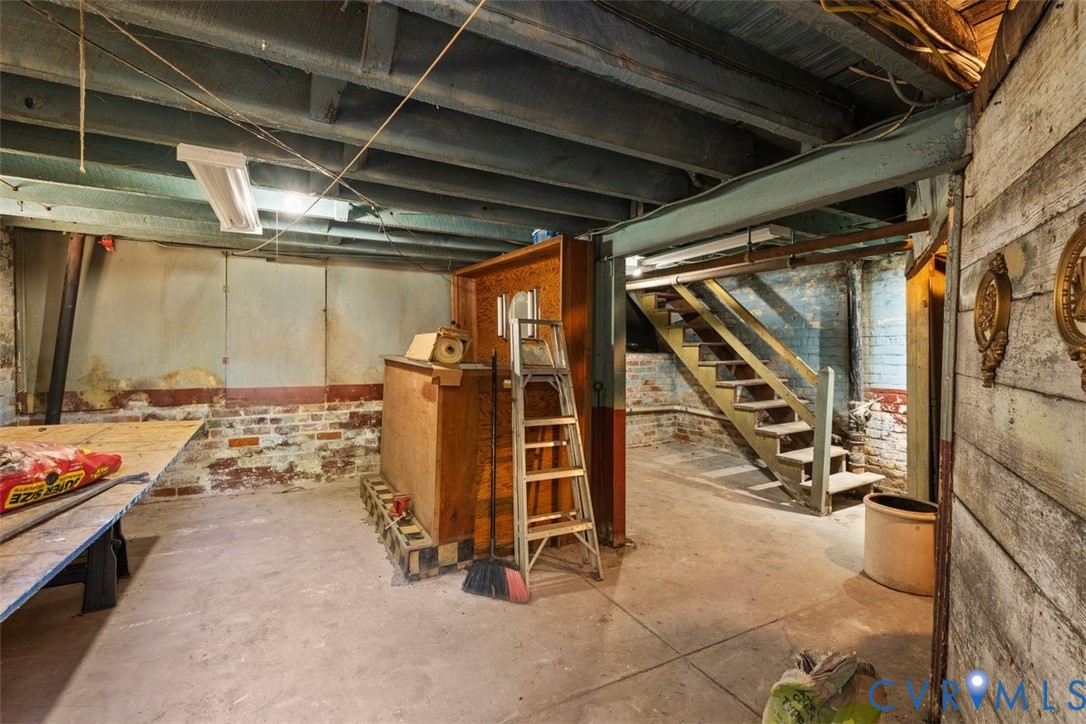 Unfinished lower level featuring exposed joist ceilings, concrete flooring, painted masonry walls, and wooden staircase