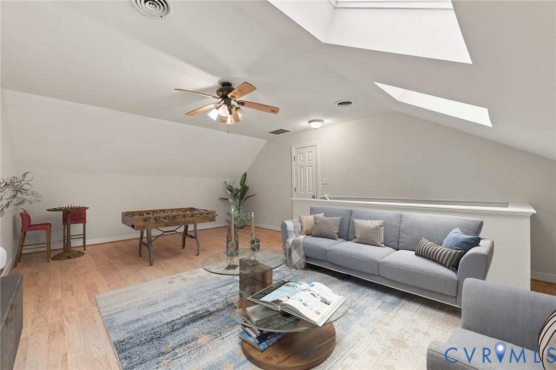 Vaulted ceilings featuring dual skylights, vinyl flooring, and a ceiling fan with integrated lighting. Virtually staged concept