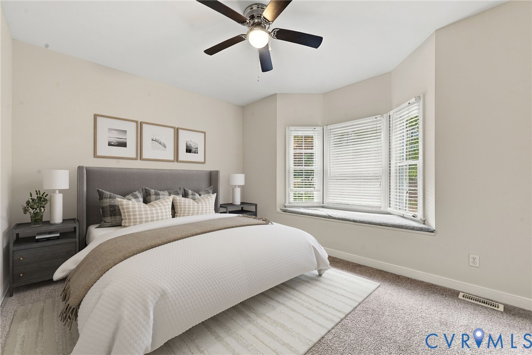 Bedroom featuring neutral wall paint, wall-to-wall carpeting, a multi-panel bay window, a built-in window seat, and a central ceiling fan with integrated lighting. Virtually staged concept