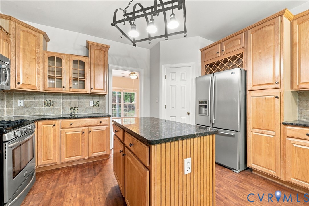 Kitchen featuring wood cabinetry, a central island with beadboard detailing, granite countertops, and stainless-steel appliances