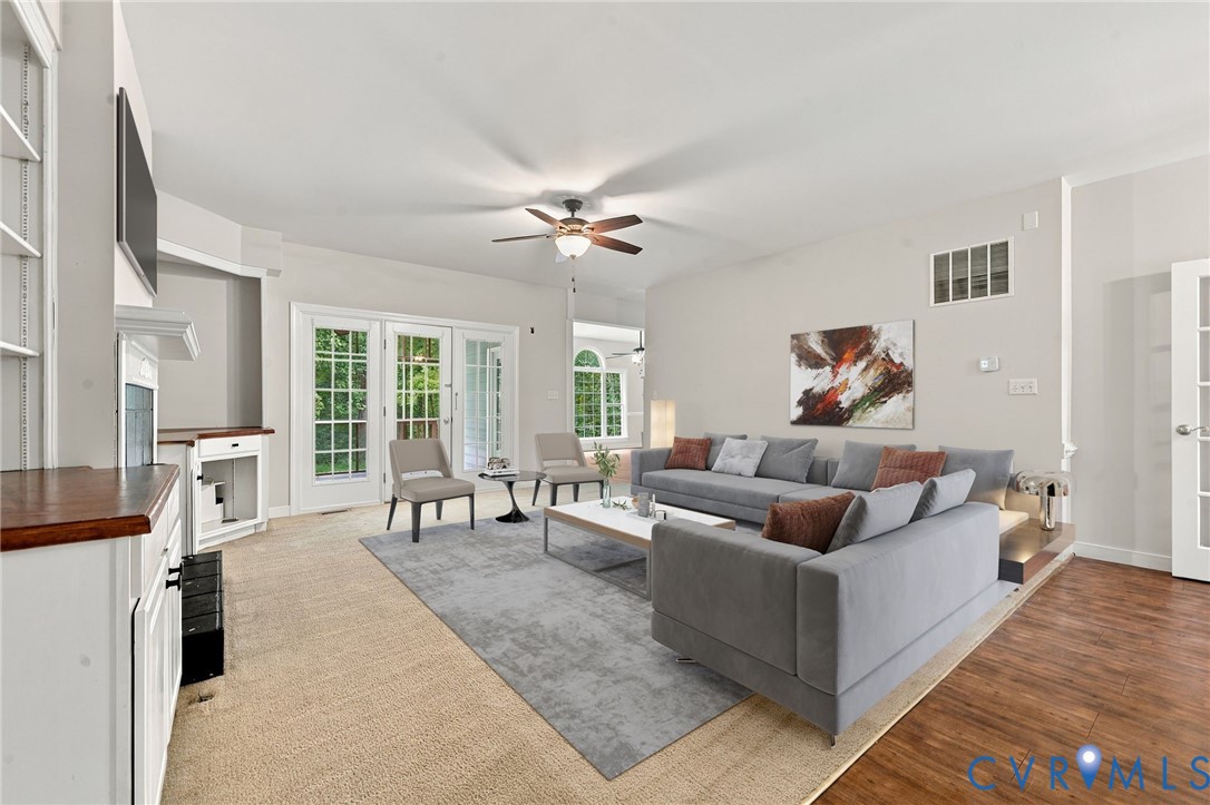 Living area featuring neutral carpeting, LVP flooring, a ceiling fan with light kit, a built-in cabinet with a wood countertop, and multi-pane glass doors. Virtually staged concept
