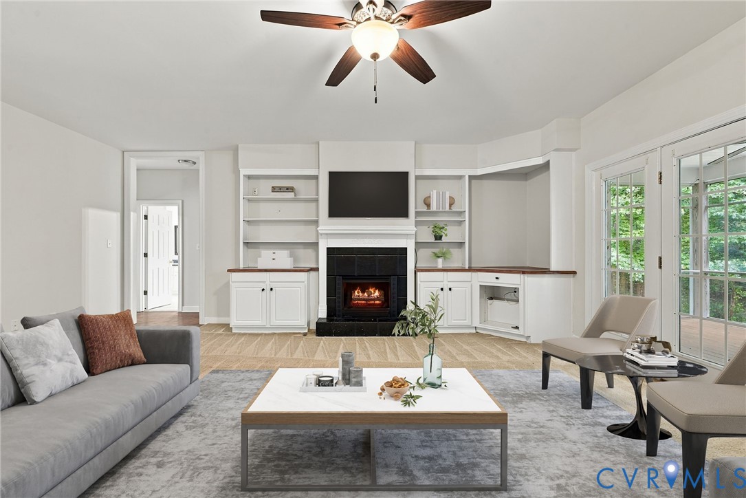 Living space featuring a central fireplace with black brick, integrated white built-in shelving, a ceiling fan with integrated lighting, and glass-paneled double doors. Virtually staged concept
