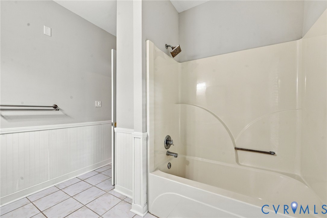 Bathroom featuring a double-vanity, white cabinetry, tile flooring, beadboard wainscoting, and a wall-mounted light fixture