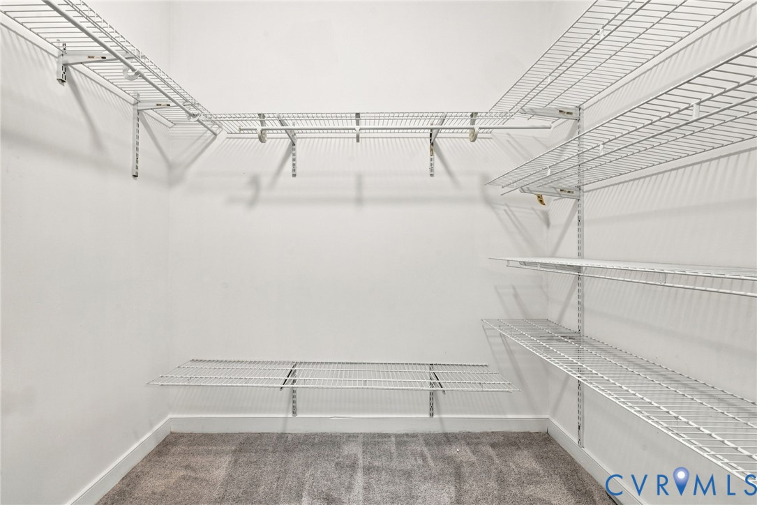Walk-in storage space featuring white wire shelving, wall-mounted supports, and neutral carpeting
