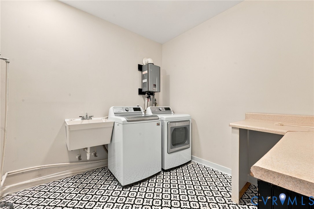 Utility space featuring a wall-mounted tankless water heater, a utility sink, patterned tile flooring, and a built-in countertop