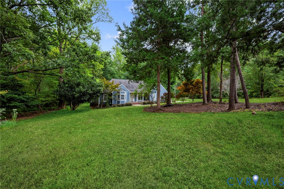 Expansive yard featuring mature trees, wooded perimeter, and a blue-siding residence with a multi-gabled roofline. Virtually edited grass