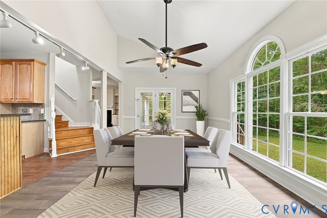Dining area featuring LVP flooring, a raised sloped ceiling, a multi-blade ceiling fan with integrated lighting, and a triple-pane window with an arched transom. Virtually staged concept