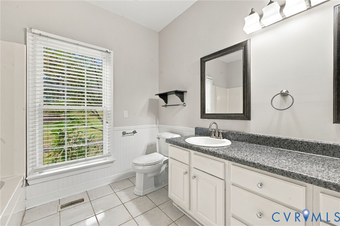 Bathroom featuring a double-vanity, white cabinetry, tile flooring, beadboard wainscoting, and a wall-mounted light fixture