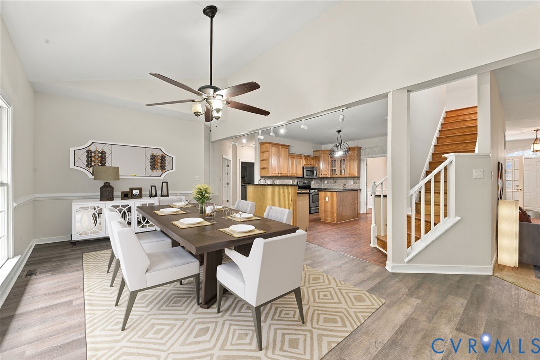Dining area featuring LVP flooring, a raised sloped ceiling, a multi-blade ceiling fan with integrated lighting, and a triple-pane window with an arched transom. Virtually staged concept