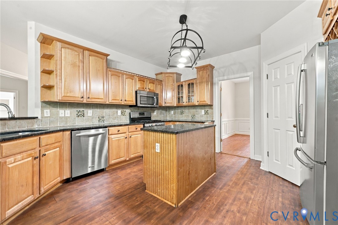 Kitchen featuring wood cabinetry, a central island with beadboard detailing, granite countertops, and stainless-steel appliances