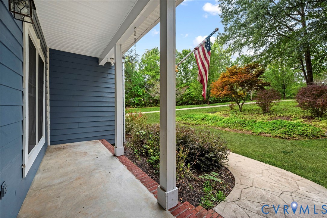Covered front porch featuring dark blue horizontal siding, white structural columns, red brick edging, and stone-paver walkway. Virtually edited grass