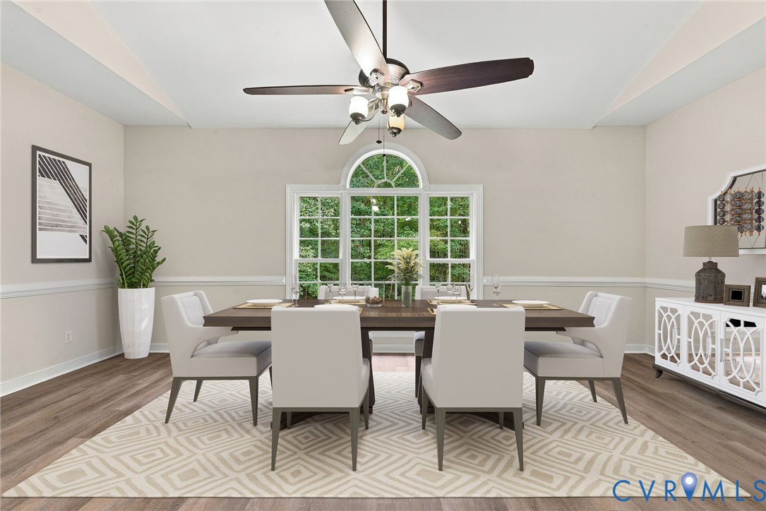 Dining area featuring LVP flooring, a raised sloped ceiling, a multi-blade ceiling fan with integrated lighting, and a triple-pane window with an arched transom. Virtually staged concept